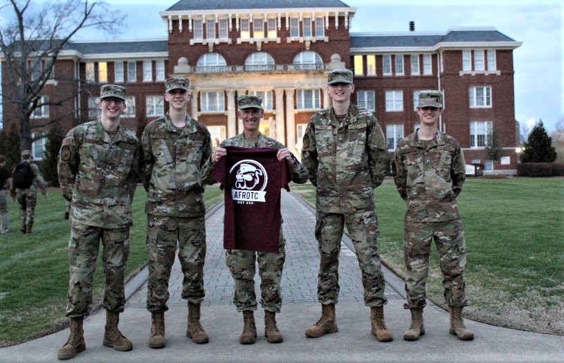 Col Bennett holding a "WarDawgs" t-shirt with two cadets on each side. 