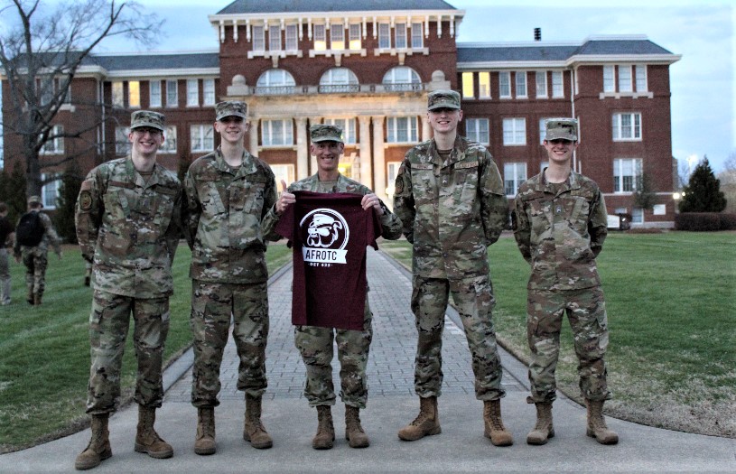 Col Bennett holding a "WarDawgs" t-shirt with two cadets on each side.
